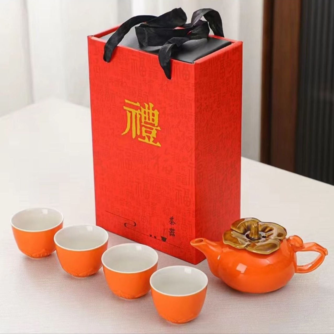 Ceramic teapot and cups set with a red gift box on a light surface.